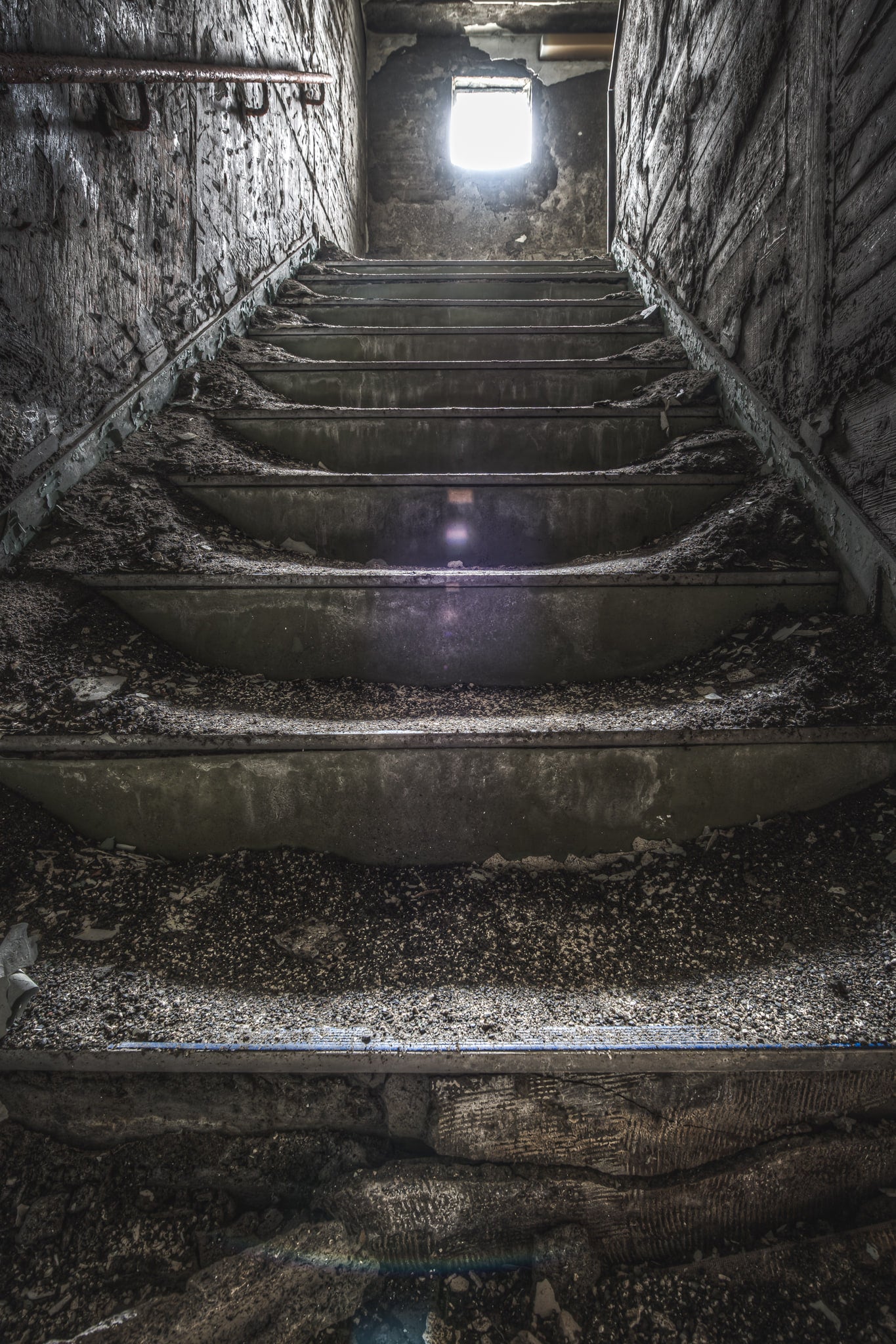 Staircase at Kuwashima Hospital, concrete steps climb a narrow stairwell toward a single bright opening.