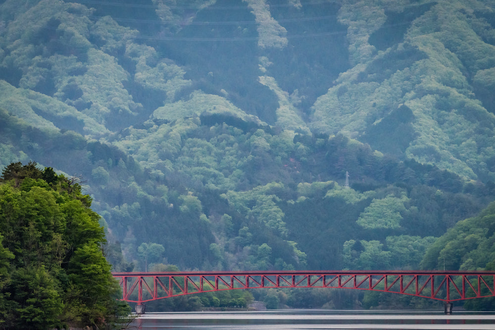 Kusaki Dam Lake at Landscapes, a red steel bridge dwarfed by mountains stretches over a lake.