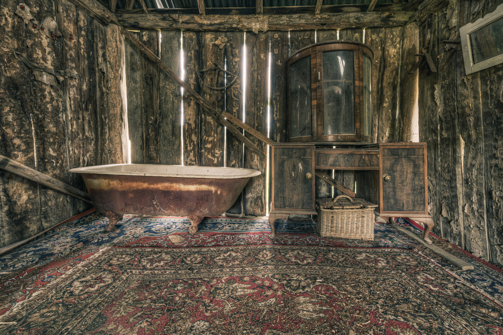 Bath at Leichhardt House, a cast-iron clawfoot bathtub sits on a Persian rug, its enamel interior stained brown with rust.