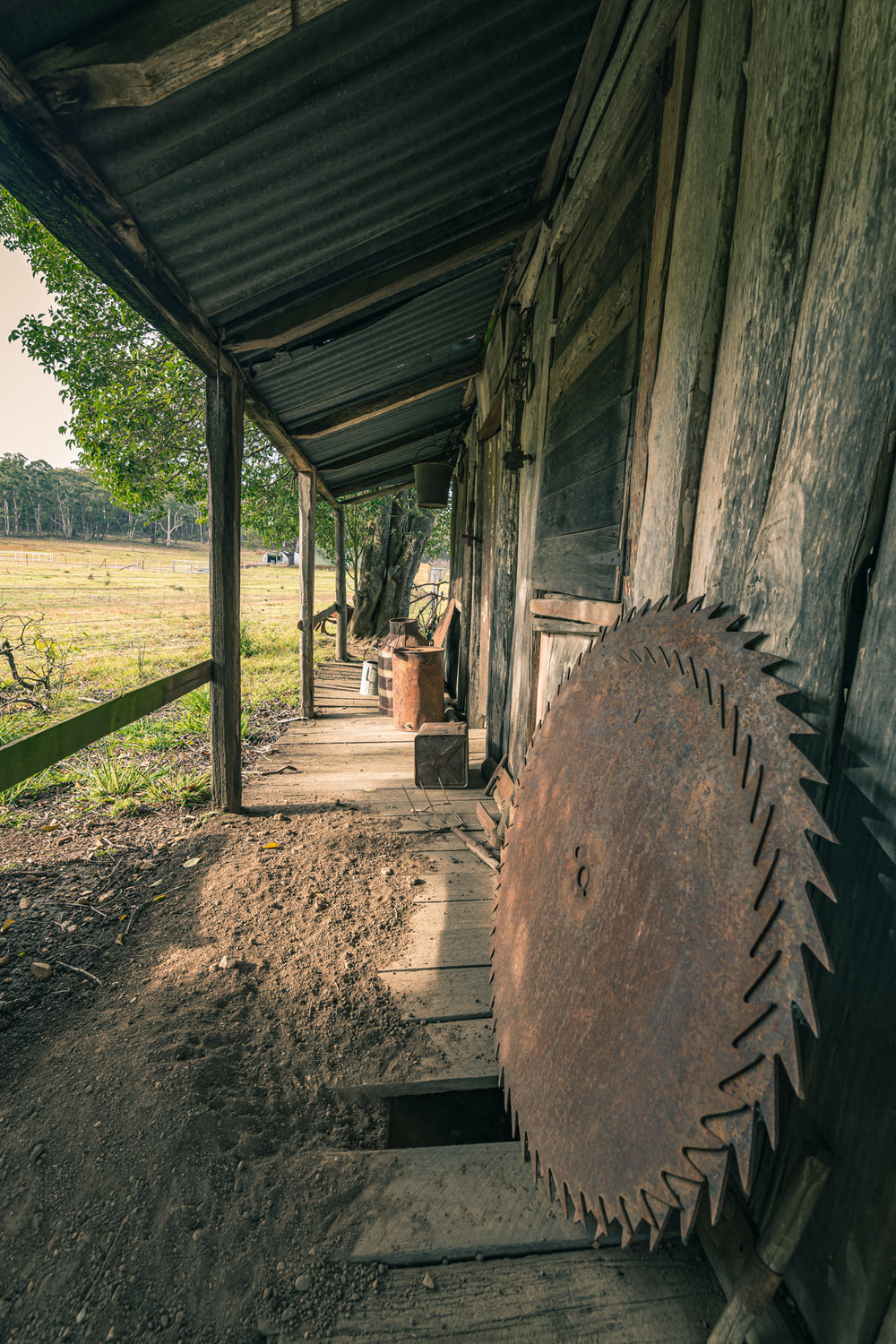 Porch Saws at Leichhardt House, a large circular saw blade leans against weathered timber cladding on a narrow verandah.