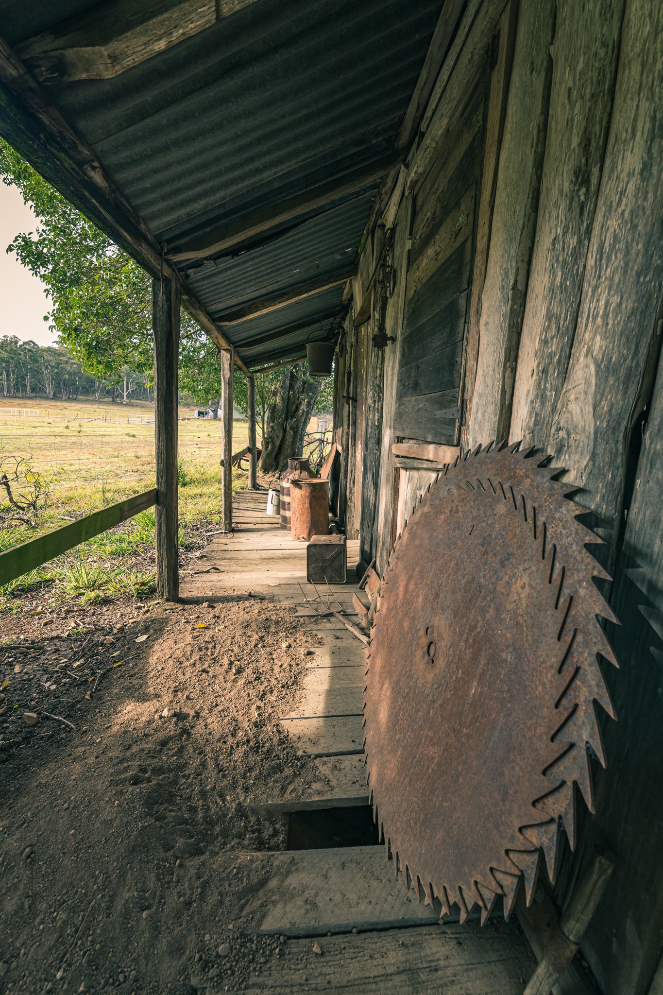 Porch Saws at Leichhardt House, a large circular saw blade leans against weathered timber cladding on a narrow verandah.