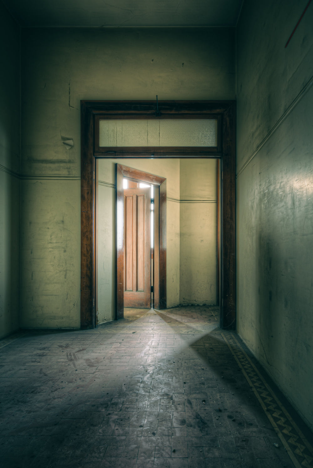 Enclave at Lewisham Hospital, a narrow corridor leads to a timber door, half-open, light pressing through the gap.
