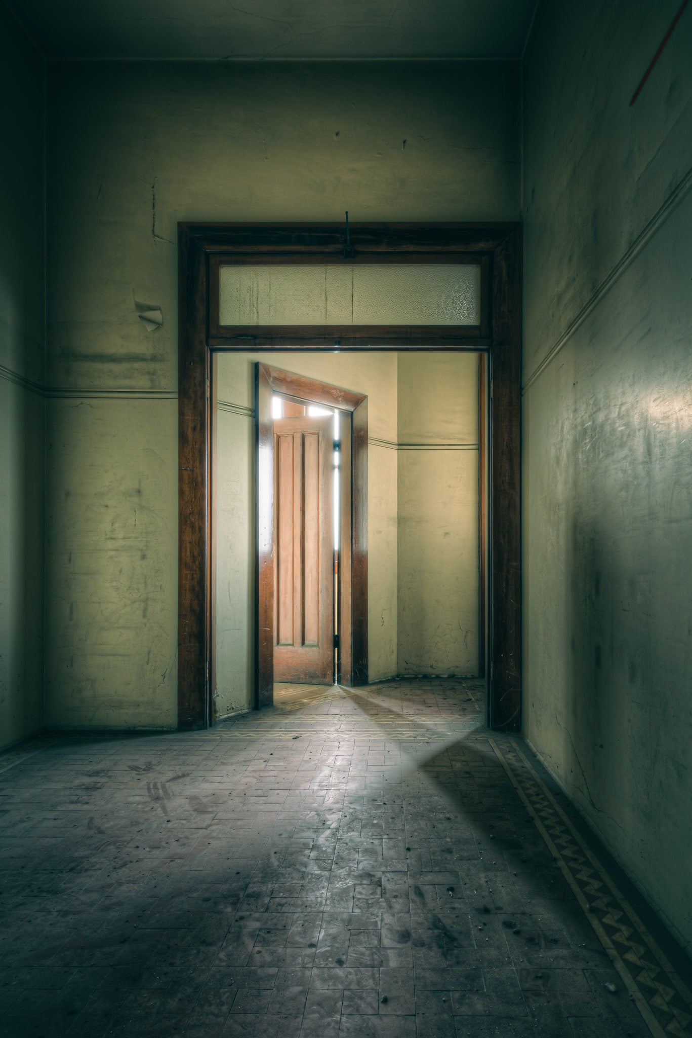 Enclave at Lewisham Hospital, a narrow corridor leads to a timber door, half-open, light pressing through the gap.