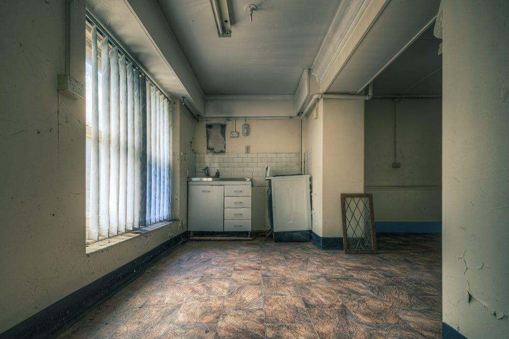 Nurses Kitchen at Lewisham Hospital, daylight pushes through vertical blinds, casting long pale strips across vinyl floor.