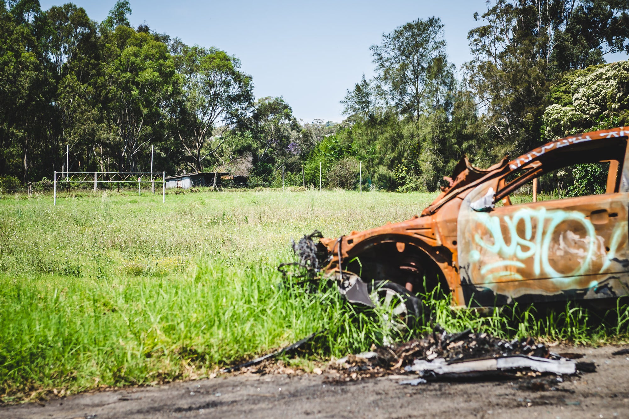 Football Field at Macquarie Boys Technology High, a burnt out car sits on the edge of the now overgrown football field.