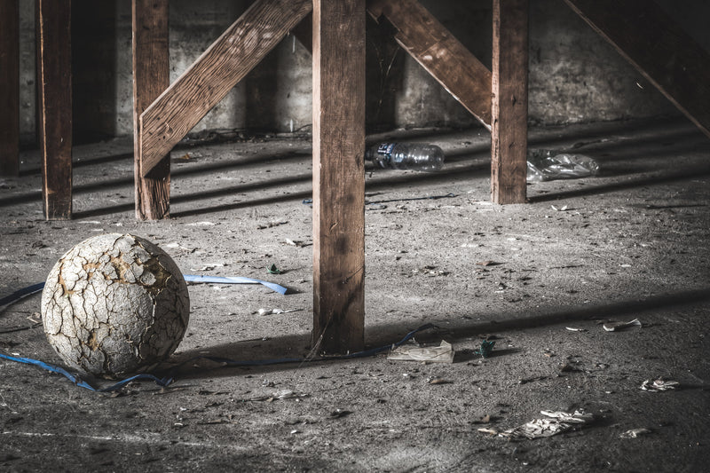 A cracked sphere, once a sports ball, sits on a dusty concrete floor with a blue strap curled around its base and 2 plastic bottles nearby at Macquarie Boys Technology High.