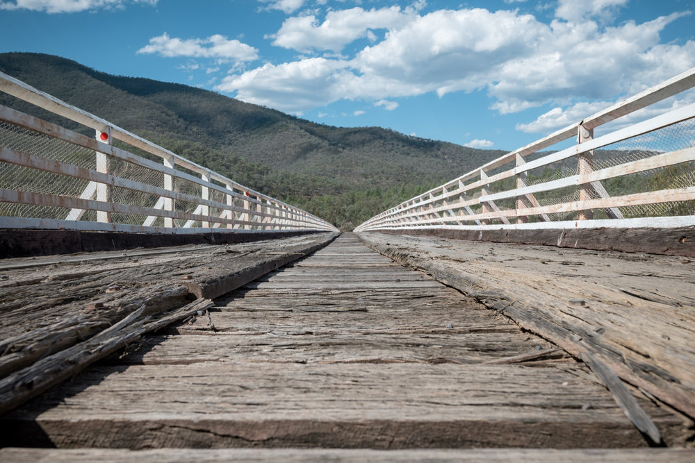 Weathered timber deck planks and white handrails recede along McKillops Bridge toward the far wall of the Snowy River gorge at Deddick Valley.