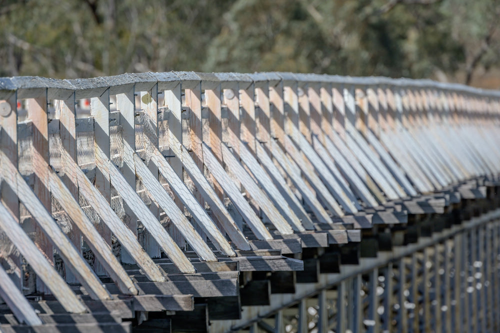 Close view along the weathered white-painted timber side railing of McKillops Bridge in the Deddick Valley, angled balusters and a diagonal top rail receding into blurred bushland.