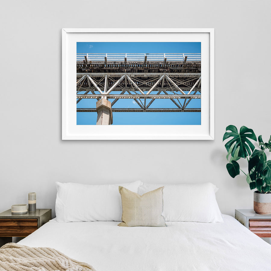 View from below McKillops Bridge in Deddick Valley, looking up at the electric-arc-welded steel Warren trusses and weathered timber decking against a clear sky, with a tall concrete pier at the left.