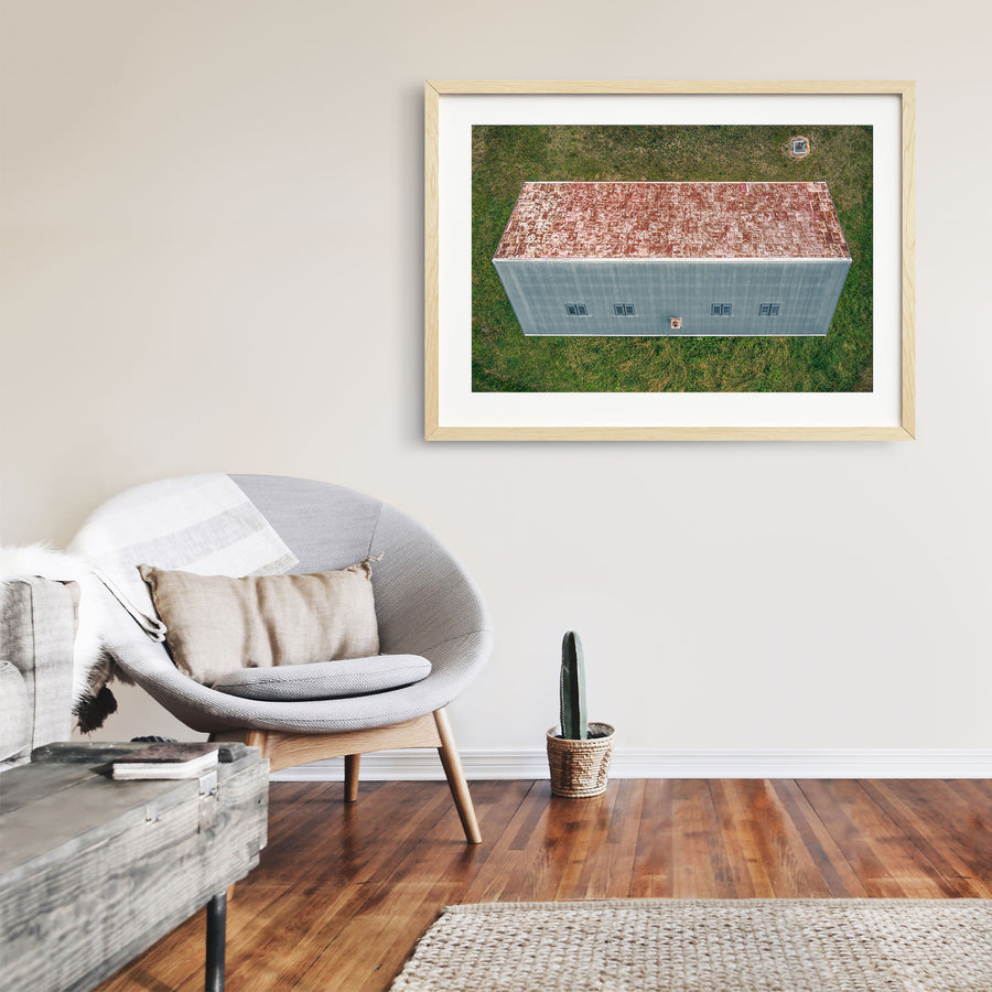 Aerial view of a long corrugated iron farm building with a rust-mottled roof and small square windows, surrounded by mown grass at Jembaicumbene.
