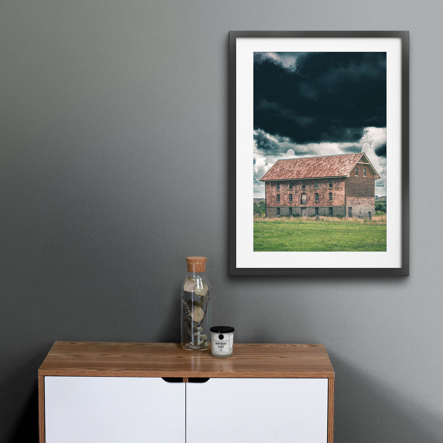 The four-storey brick and granite flour mill at Jembaicumbene, its multi-paned windows and central iron balcony visible against a heavy grey sky, photographed in open grassland near Braidwood.