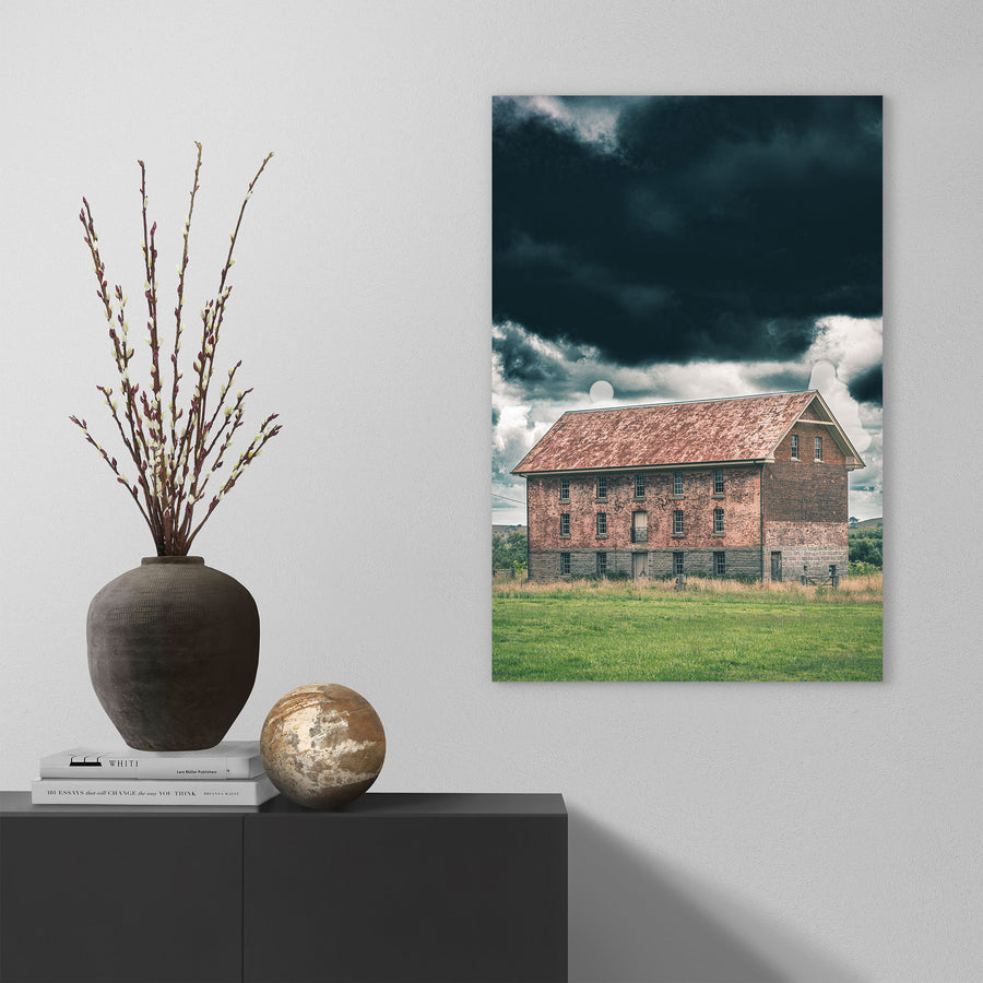 The four-storey brick and granite flour mill at Jembaicumbene, its multi-paned windows and central iron balcony visible against a heavy grey sky, photographed in open grassland near Braidwood.
