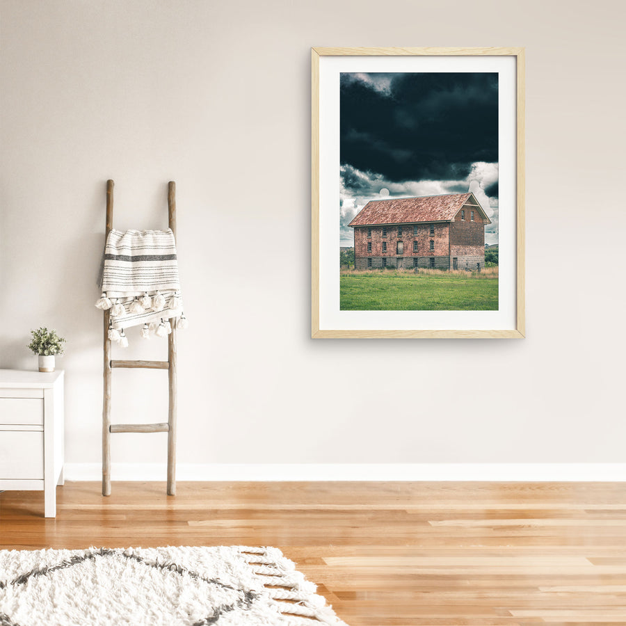 The four-storey brick and granite flour mill at Jembaicumbene, its multi-paned windows and central iron balcony visible against a heavy grey sky, photographed in open grassland near Braidwood.