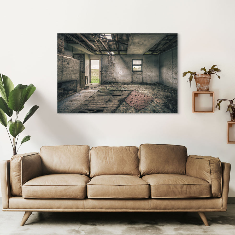 Interior of a derelict room at Jembaicumbene with a partly collapsed corrugated metal roof open to the sky, exposed timber rafters, rendered walls, a four-pane sash window, an open timber door to a paddock, and a torn red rug on broken floorboards.