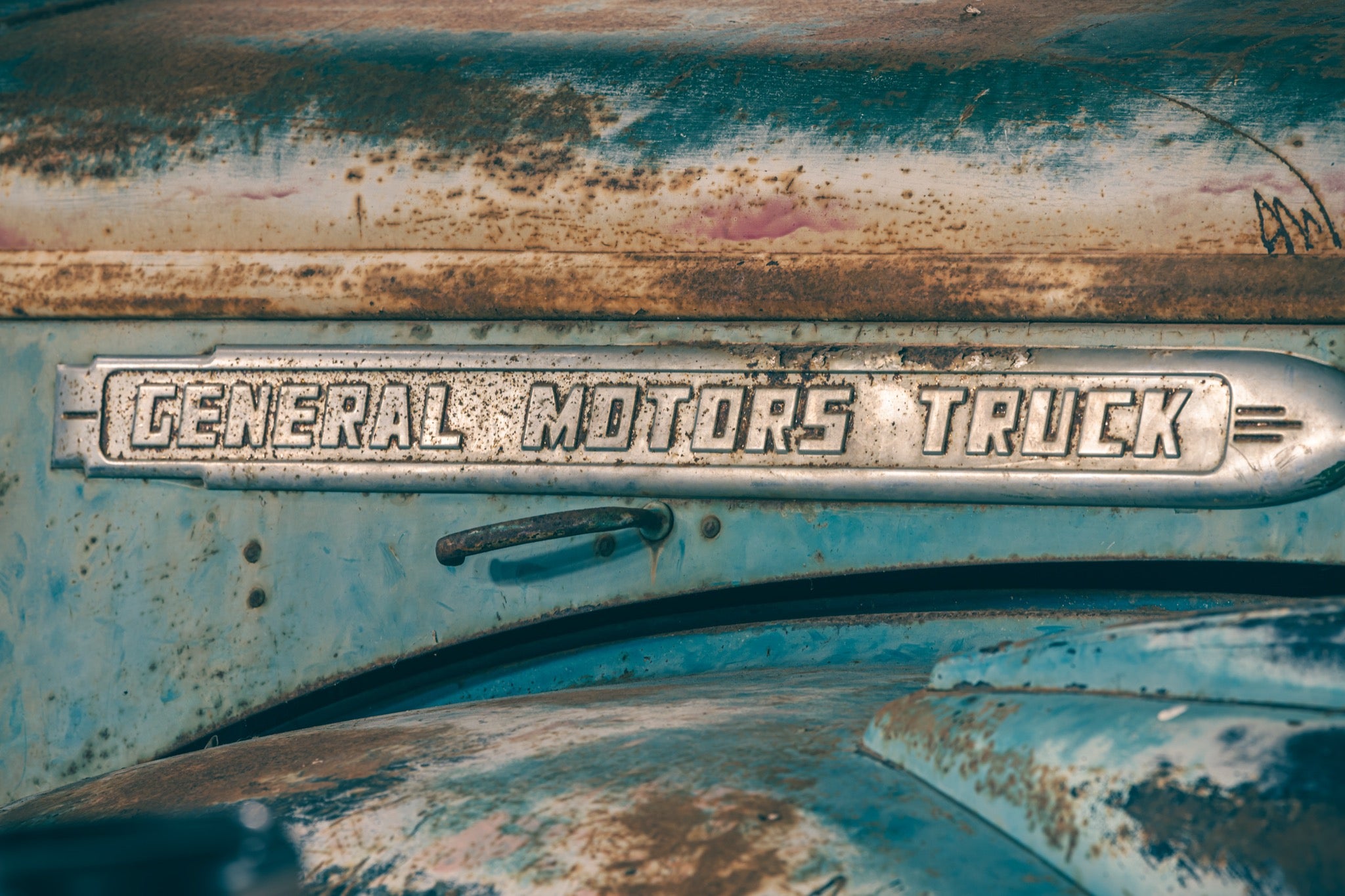 A rust-spotted General Motors Truck nameplate on a weathered blue vehicle panel with flaking paint, photographed at Jembaicumbene.