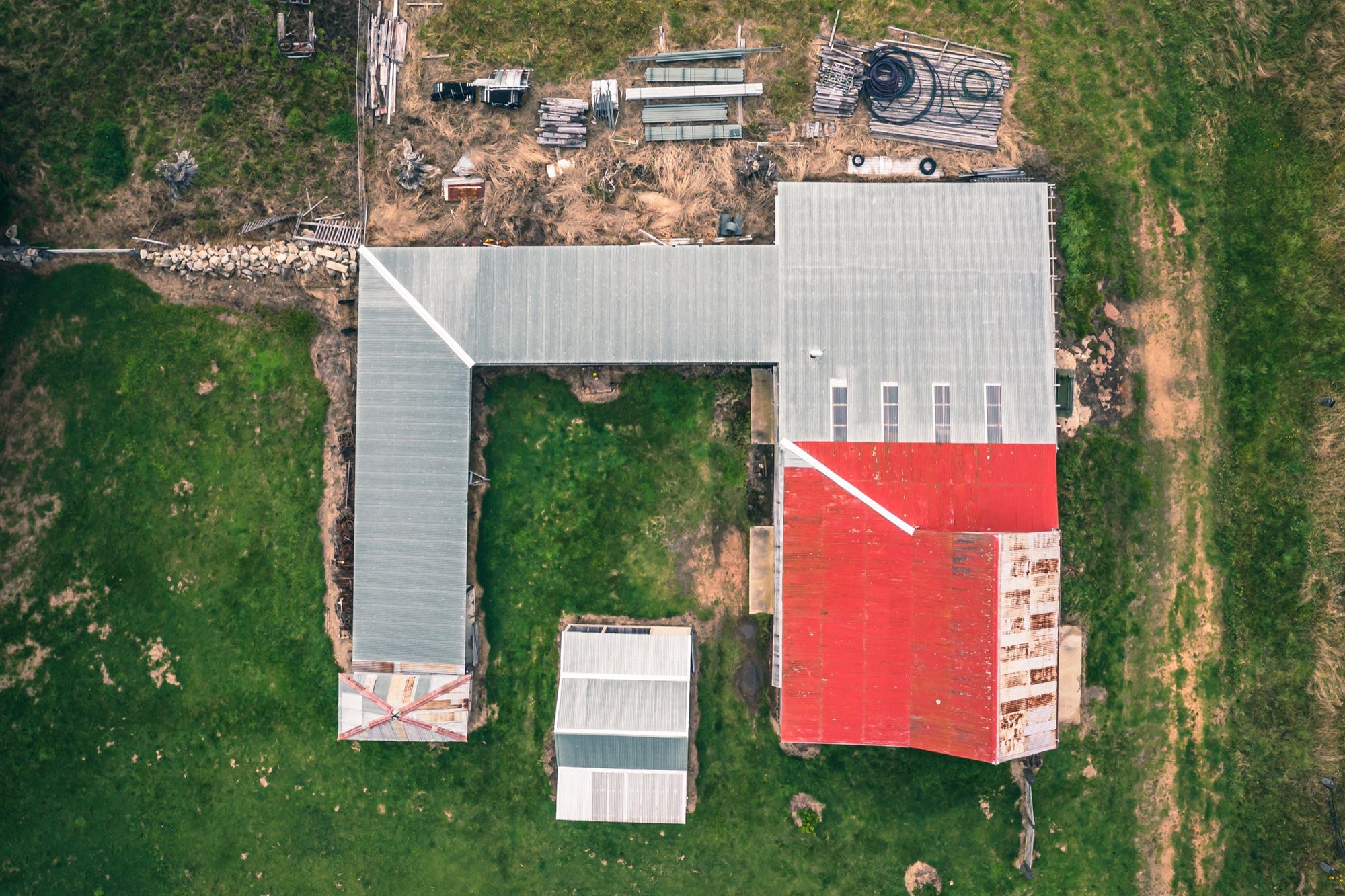 Aerial view of an L-shaped farm complex with grey and red corrugated iron roofing, surrounded by green paddocks at Jembaicumbene, New South Wales.