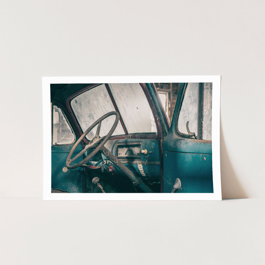 A dust-covered steering wheel and faded blue dashboard with a round gauge cluster inside an abandoned truck cab at Jembaicumbene.
