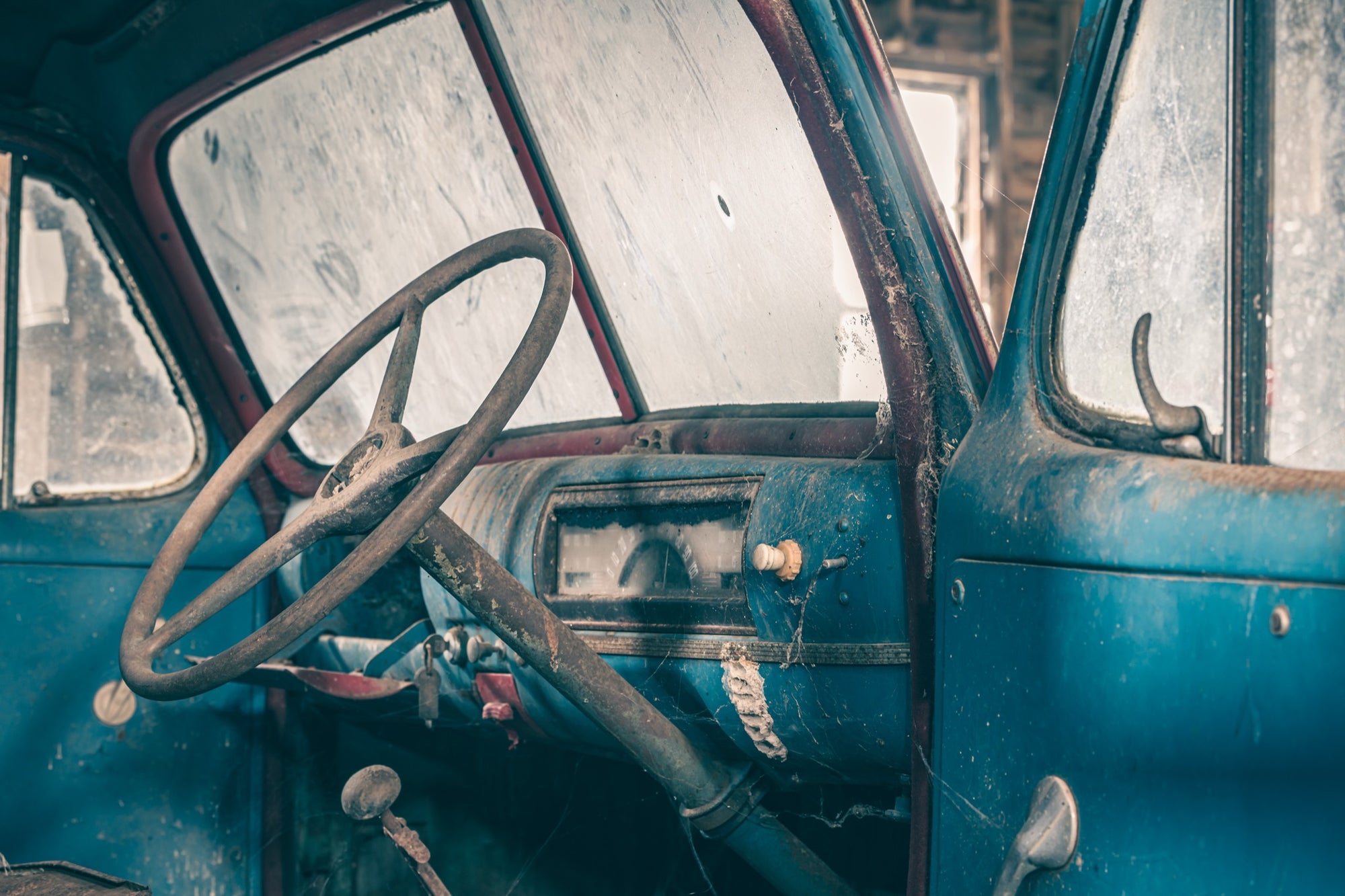 A dust-covered steering wheel and faded blue dashboard with a round gauge cluster inside an abandoned truck cab at Jembaicumbene.