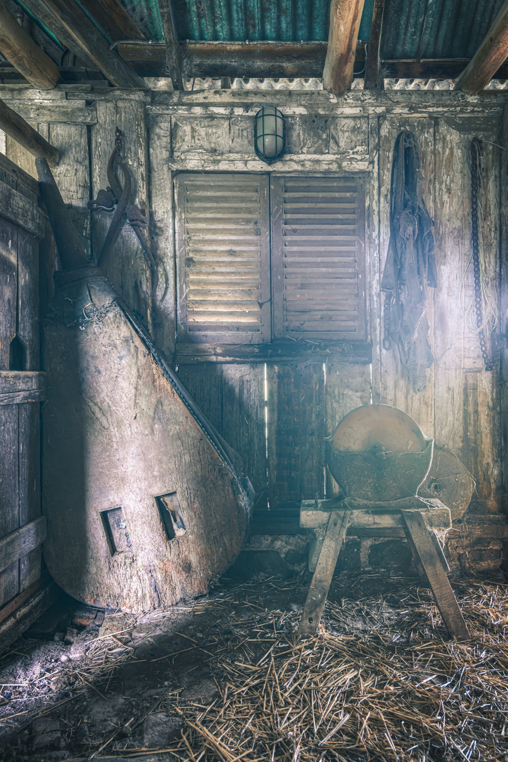 Shed interior at Jembaicumbene, a stone grindstone on a timber frame beside a conical metal vessel.