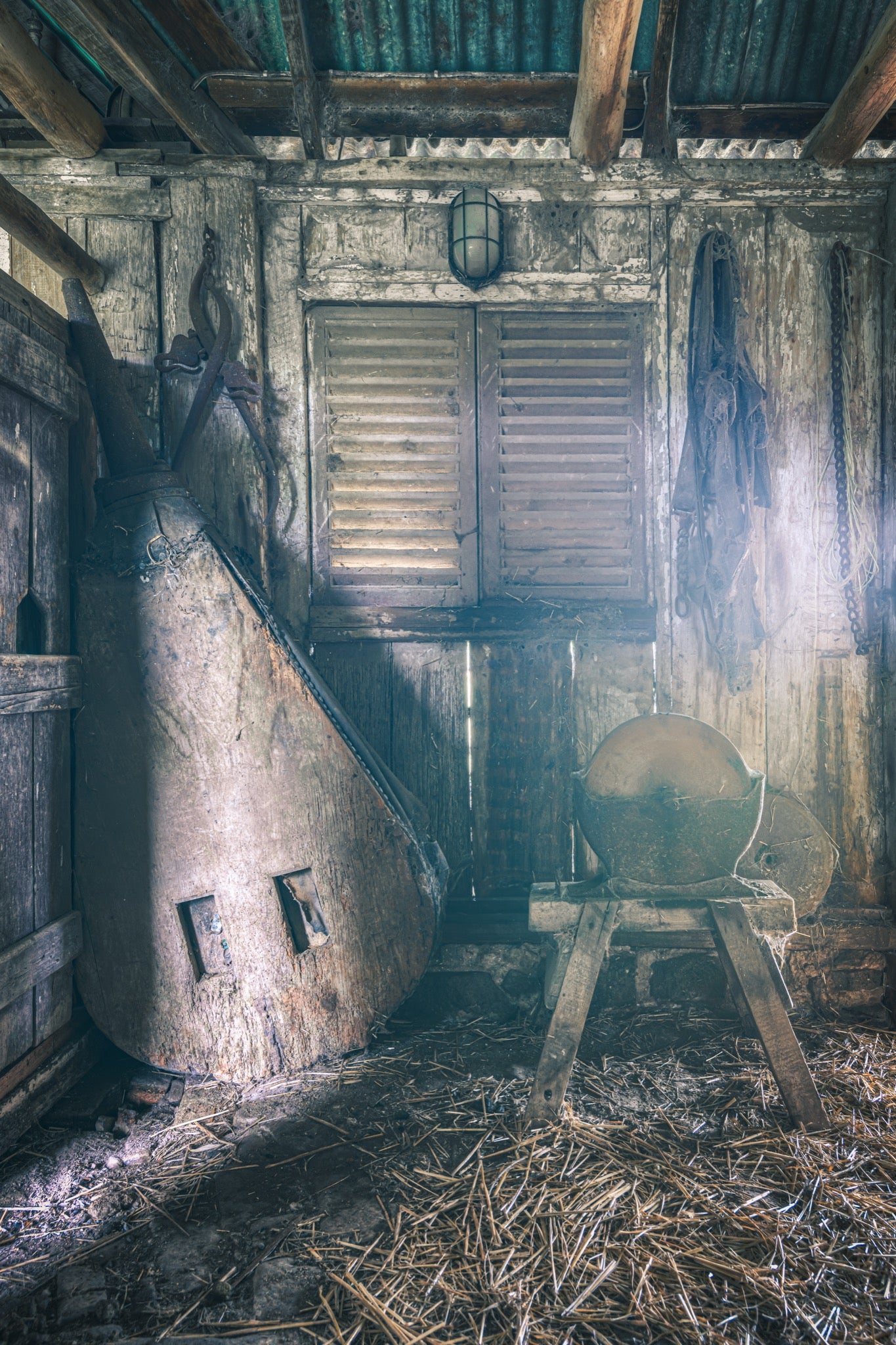 Shed interior at Jembaicumbene, a stone grindstone on a timber frame beside a conical metal vessel.