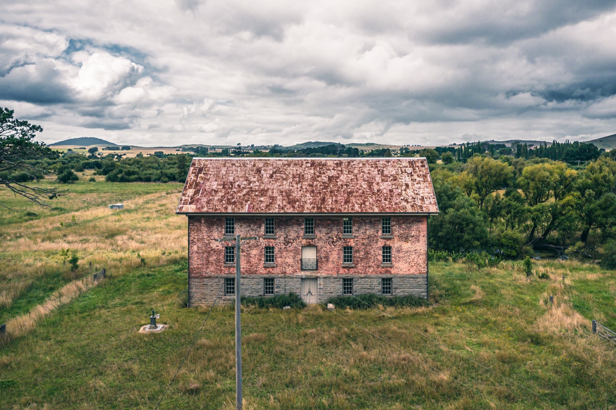 Three storey mill at Jembaicumbene, stone base under brick walls and a rusting pitched roof.