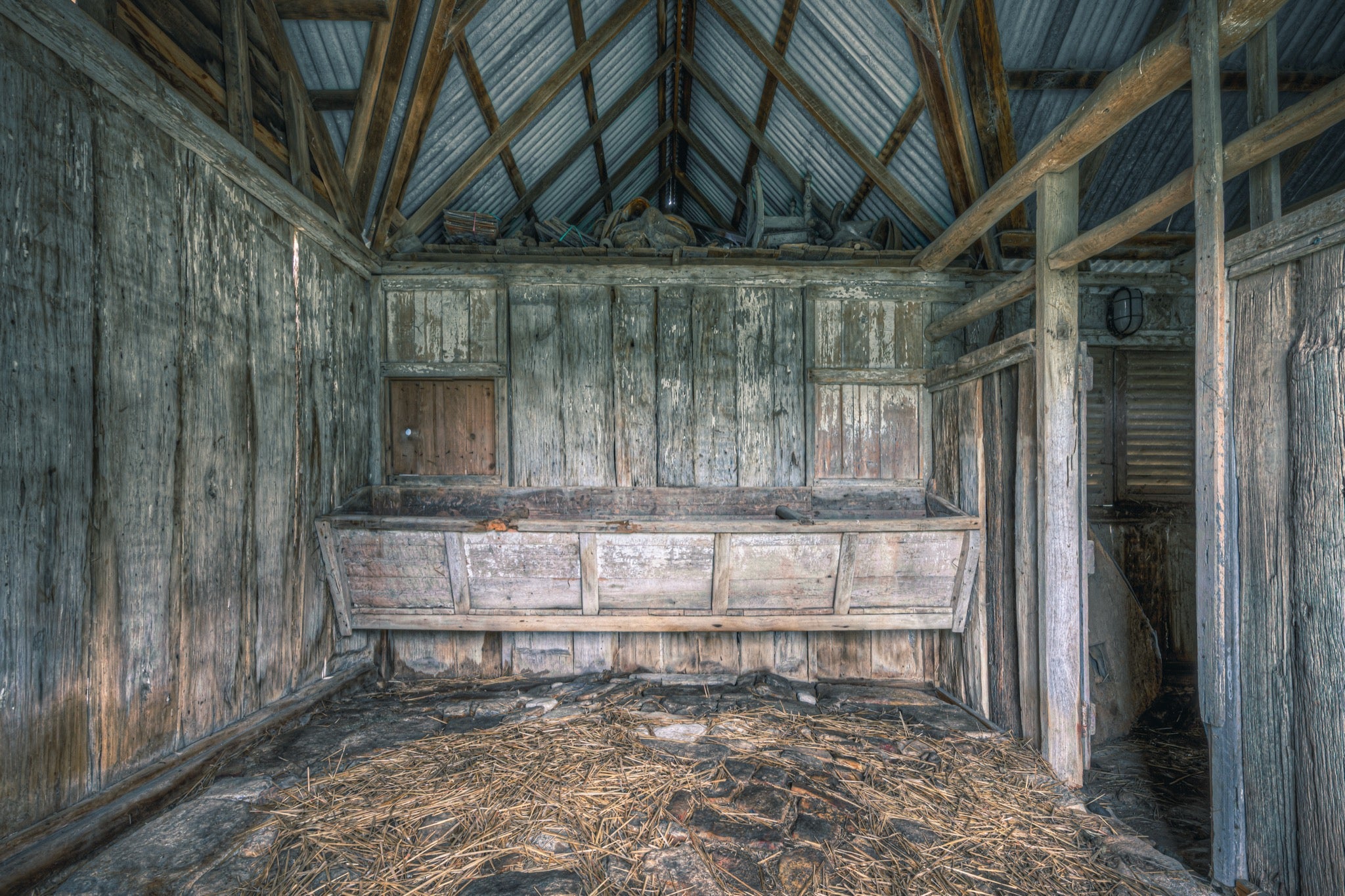 Feed trough and timber walls at Jembaicumbene barn, straw scattered across the dirt floor.