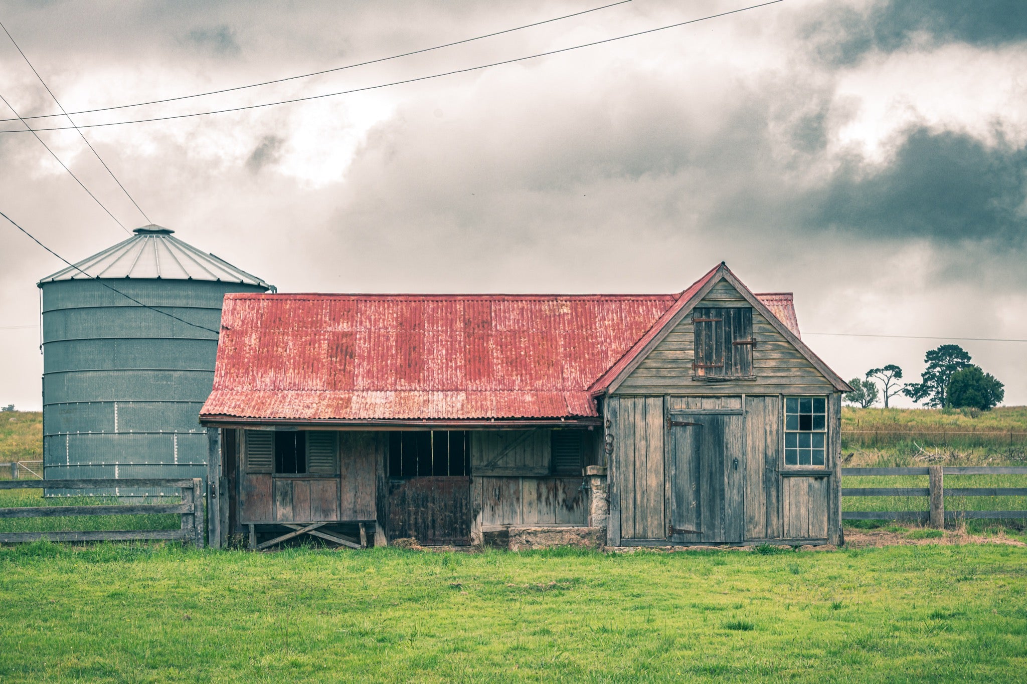 Timber stable at Braidwood, rusting red iron roof beside a tall grey grain silo.