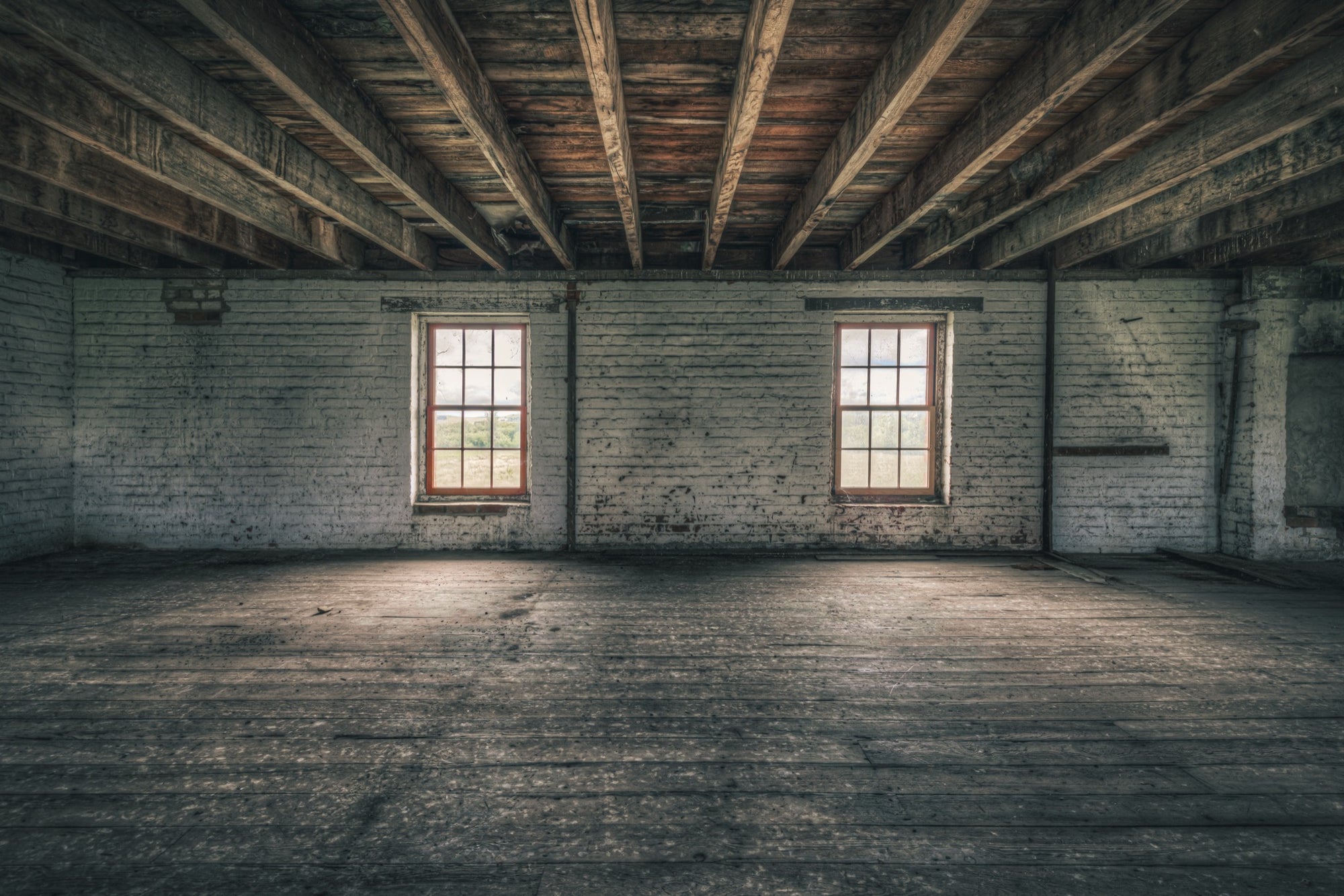 Upper room at Jembaicumbene grain store, two sash windows in a whitewashed brick wall under timber beams.