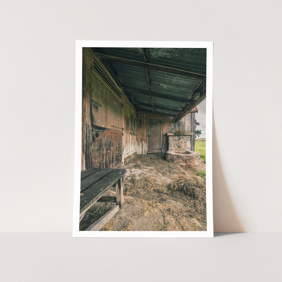 Covered timber walkway at Jembaicumbene, peeling red plank wall beside a stone trough.