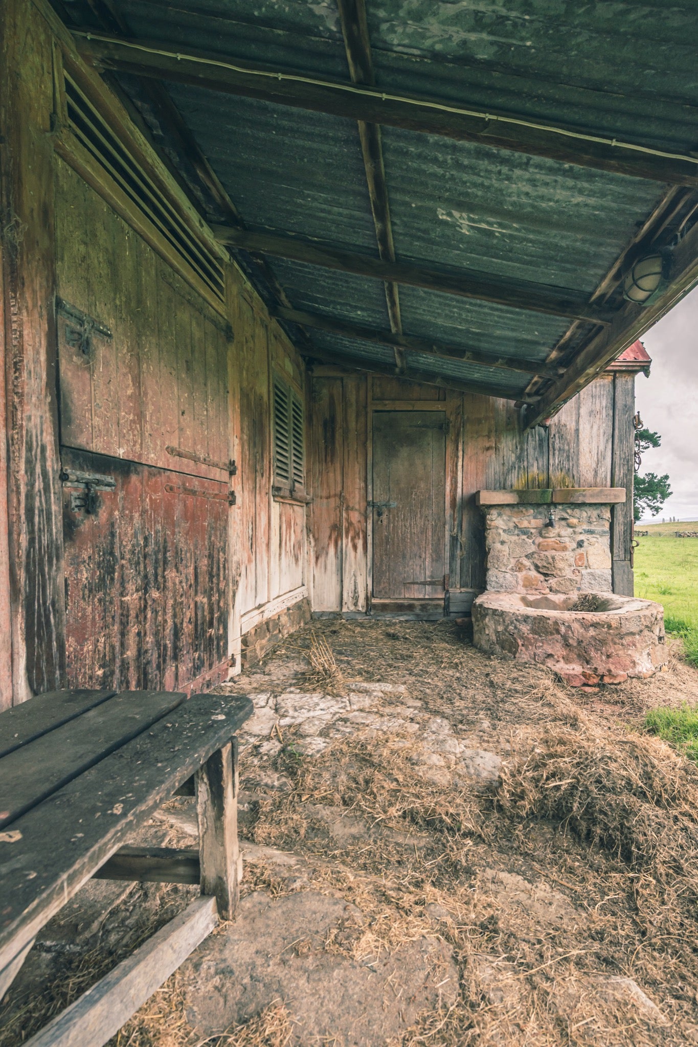 Covered timber walkway at Jembaicumbene, peeling red plank wall beside a stone trough.