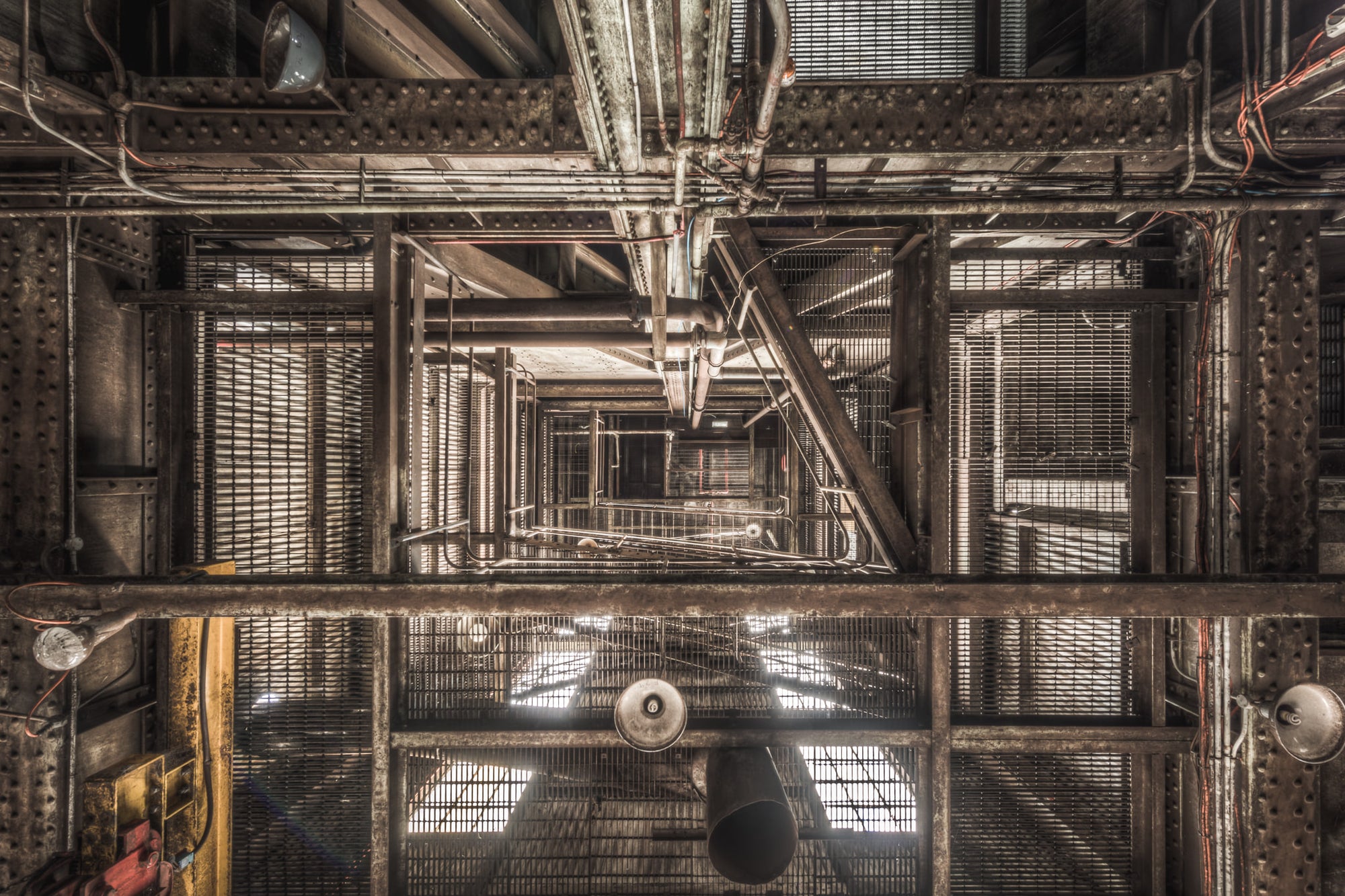 Ascent at Morwell Power Station, steel grating and riveted iron columns stack upward through multiple levels, viewed.