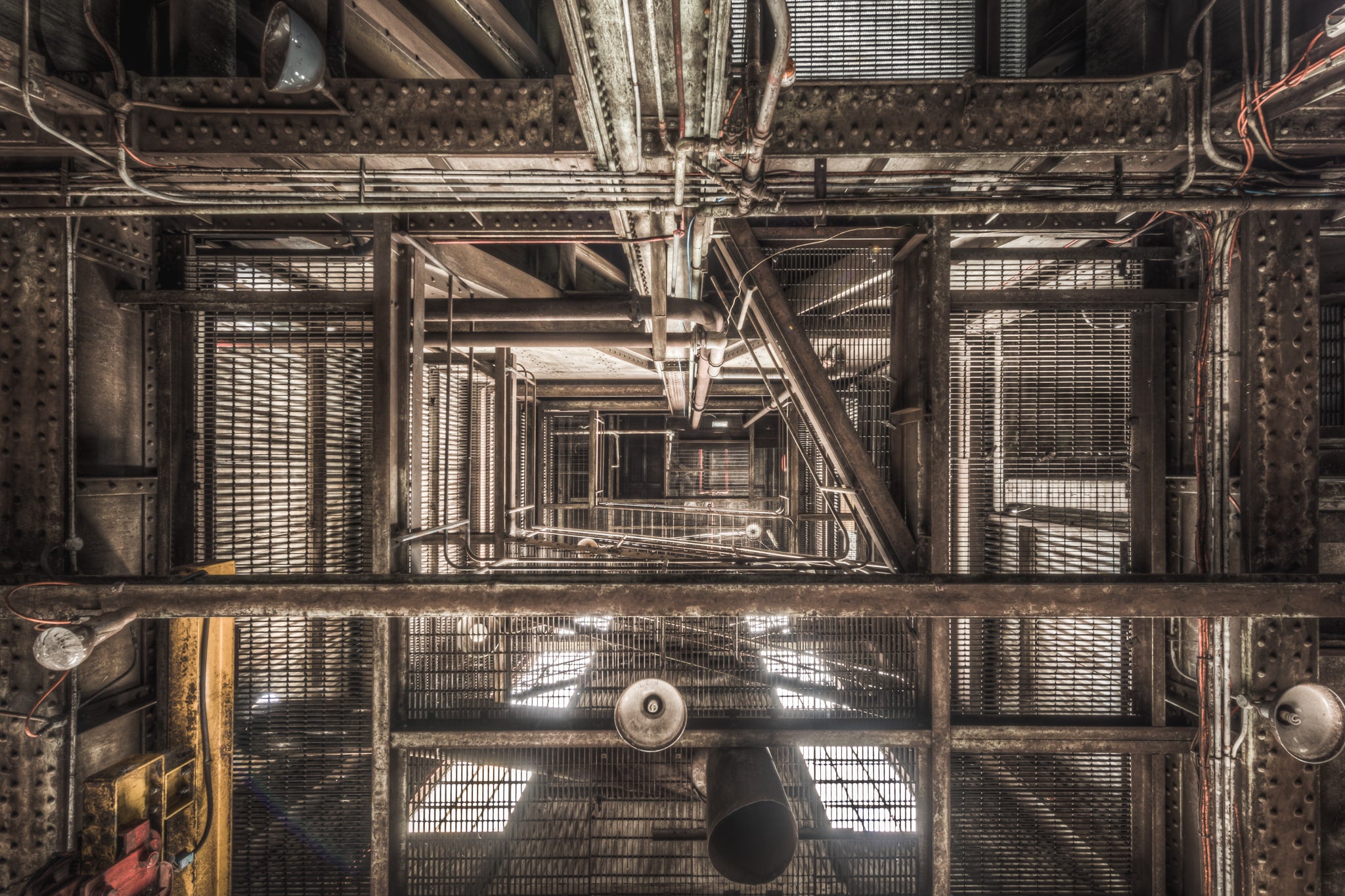 Ascent at Morwell Power Station, steel grating and riveted iron columns stack upward through multiple levels, viewed.
