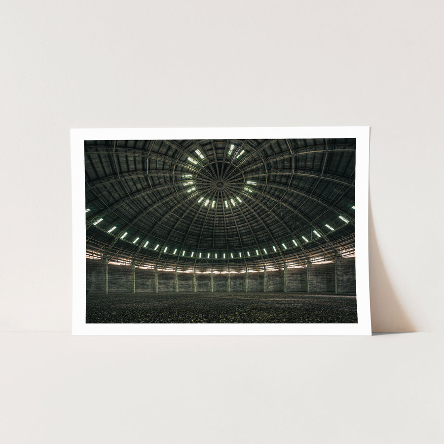 View looking up at the steel-framed dome interior of the grain silo at Mount Russell, with concentric skylight openings and a gravel-covered floor below.
