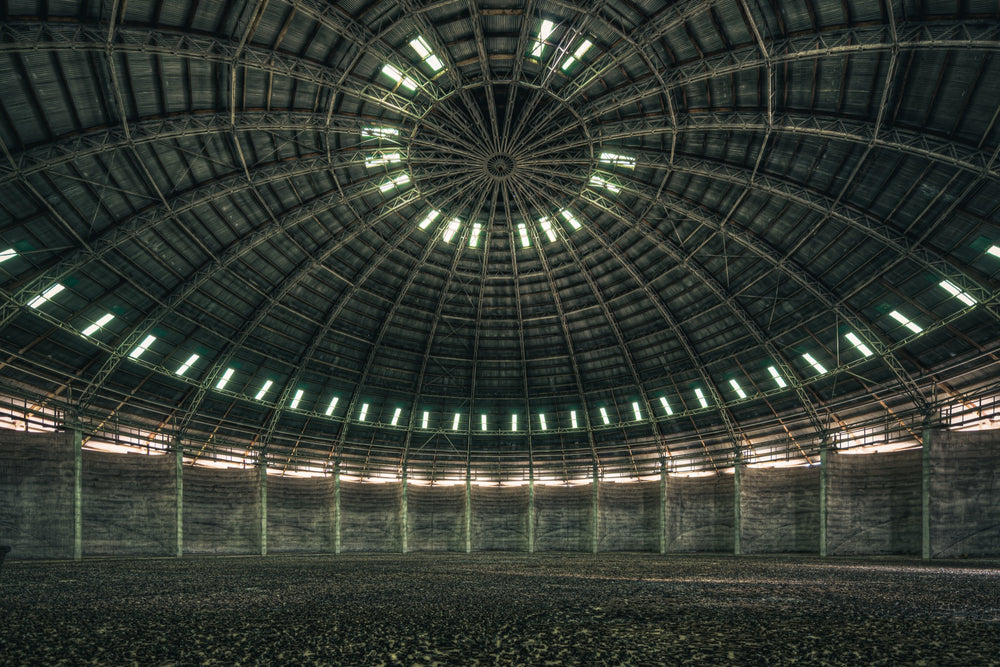 View looking up at the steel-framed dome interior of the grain silo at Mount Russell, with concentric skylight openings and a gravel-covered floor below.
