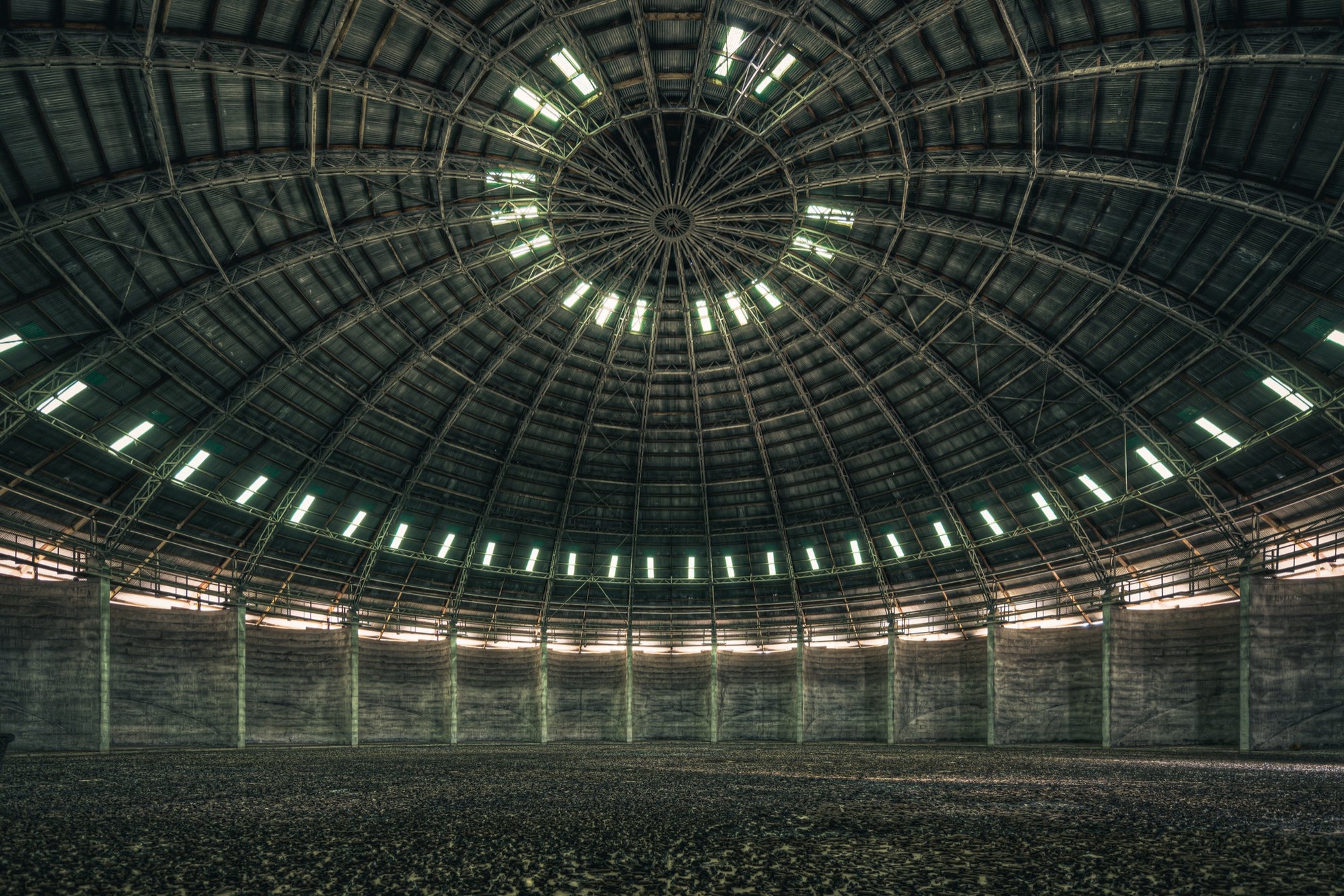 View looking up at the steel-framed dome interior of the grain silo at Mount Russell, with concentric skylight openings and a gravel-covered floor below.