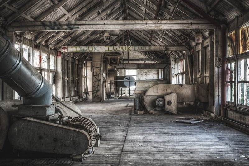 The top floor of the Mungo Scott Flour Mill, where a large angled grey pipe fills the left foreground and a pale industrial fan or air handler sits to the right beside exposed timber beams.