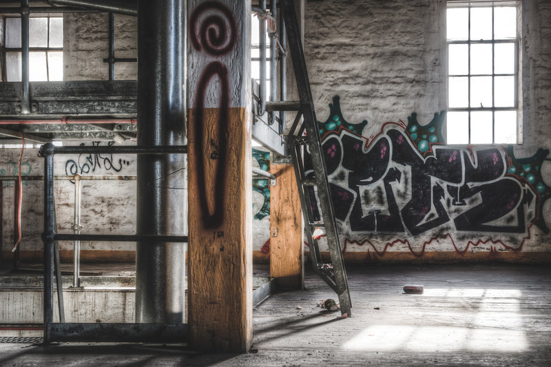 A mezzanine level within the Mungo Scott Flour Mill at Summer Hill. Dust coats the concrete floor and the machinery. Natural light enters through high windows set into brick walls. The structural frame is visible in the background.