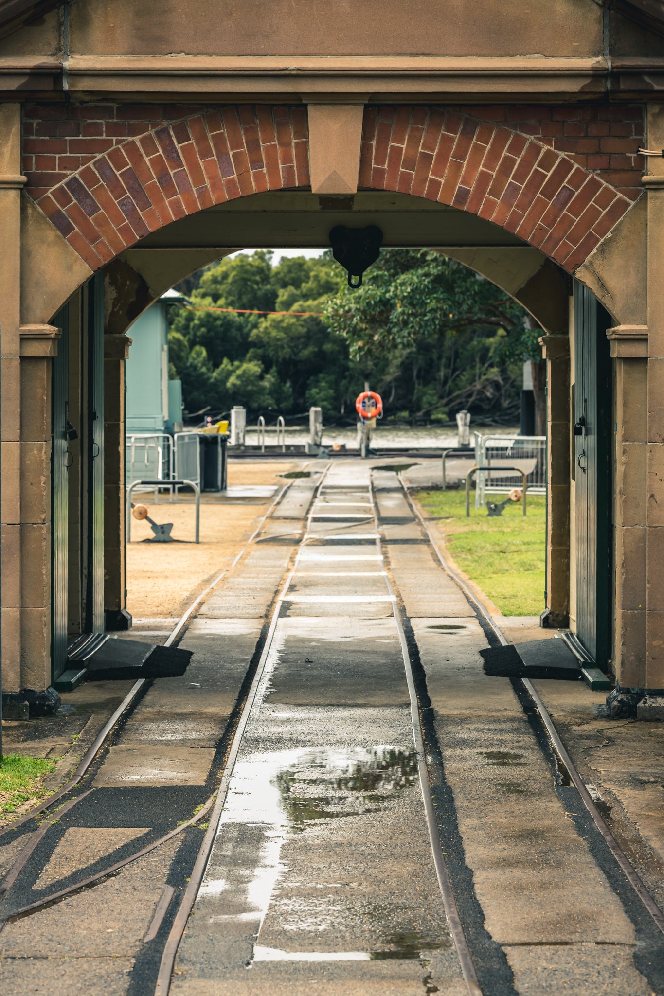 Entrance Rails at Newington Armory, narrow-gauge rail tracks run wet through a sandstone and brick archway, heading.