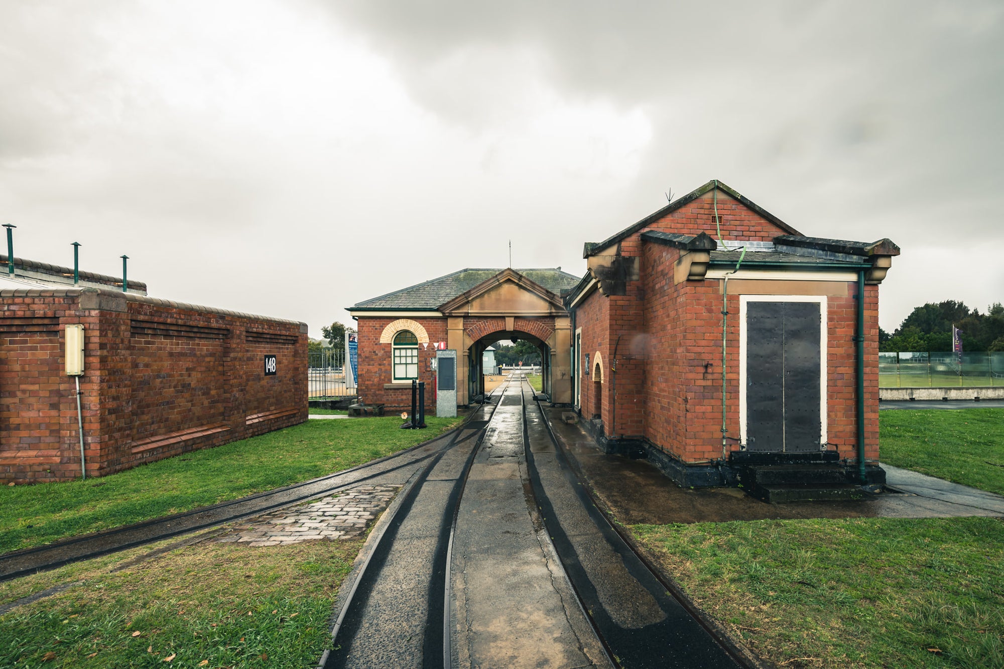 Entrance at Newington Armory, narrow-gauge rail lines run wet and black through a formal brick gatehouse at Newington Armory.