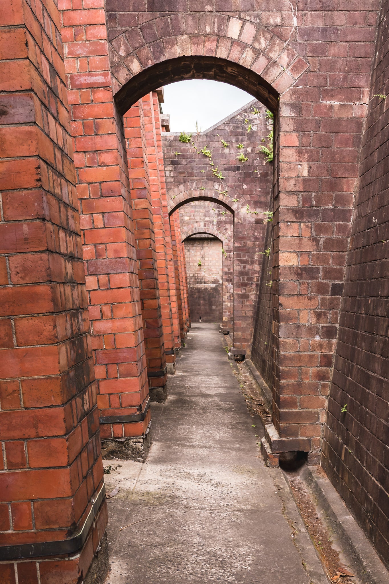 Magazine Exterior Path at Newington Armory, a narrow concrete path runs between two massive brick walls.