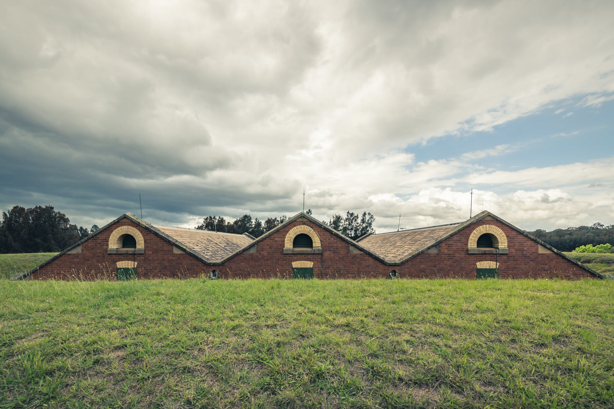 Magazine Roof at Newington Armory, three sawtooth rooflines rise from an earth embankment, red brick gables barely clearing.