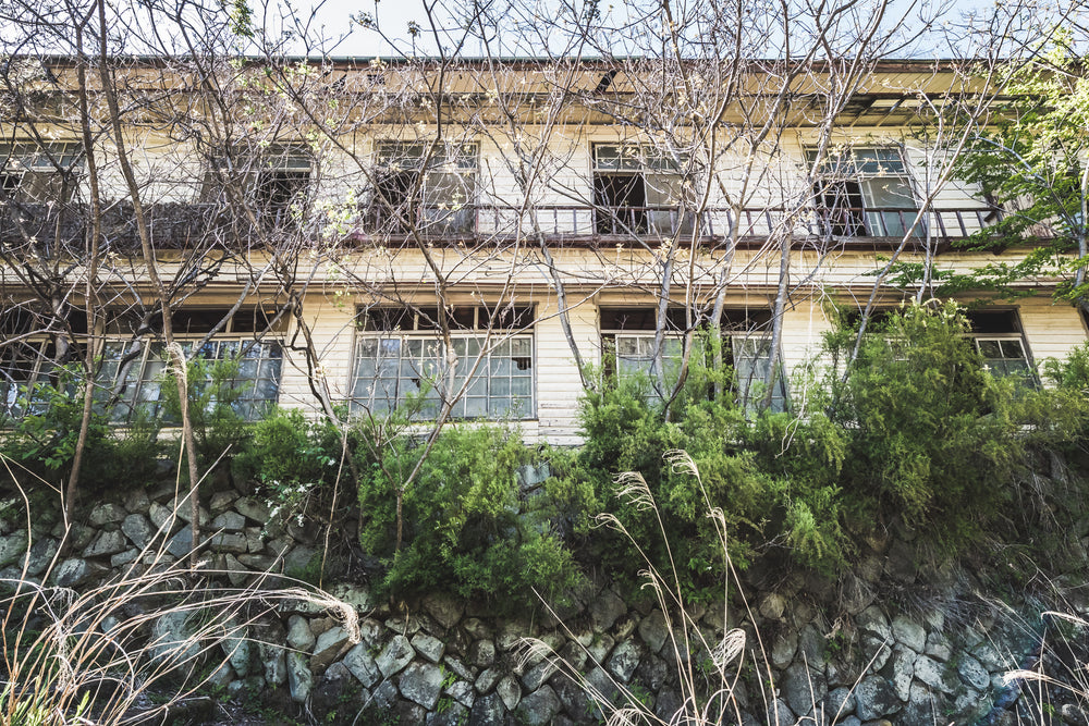 Balcony at Nichitsu Mining Village, a two-storey timber building rises behind a rough stone retaining wall.
