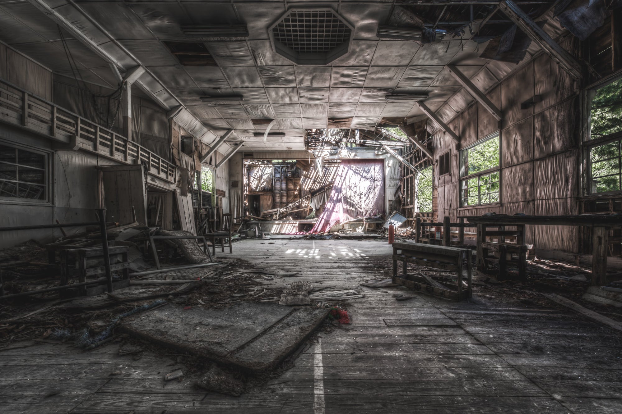 Theatre at Nichitsu Mining Village, a collapsed stage curtain hangs in shreds at the far end of the hall.