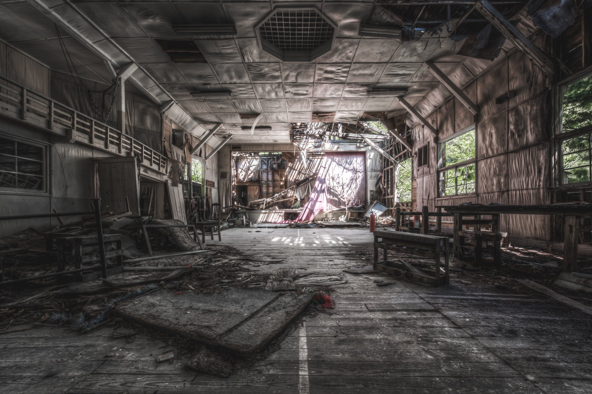 Theatre at Nichitsu Mining Village, a collapsed stage curtain hangs in shreds at the far end of the hall.