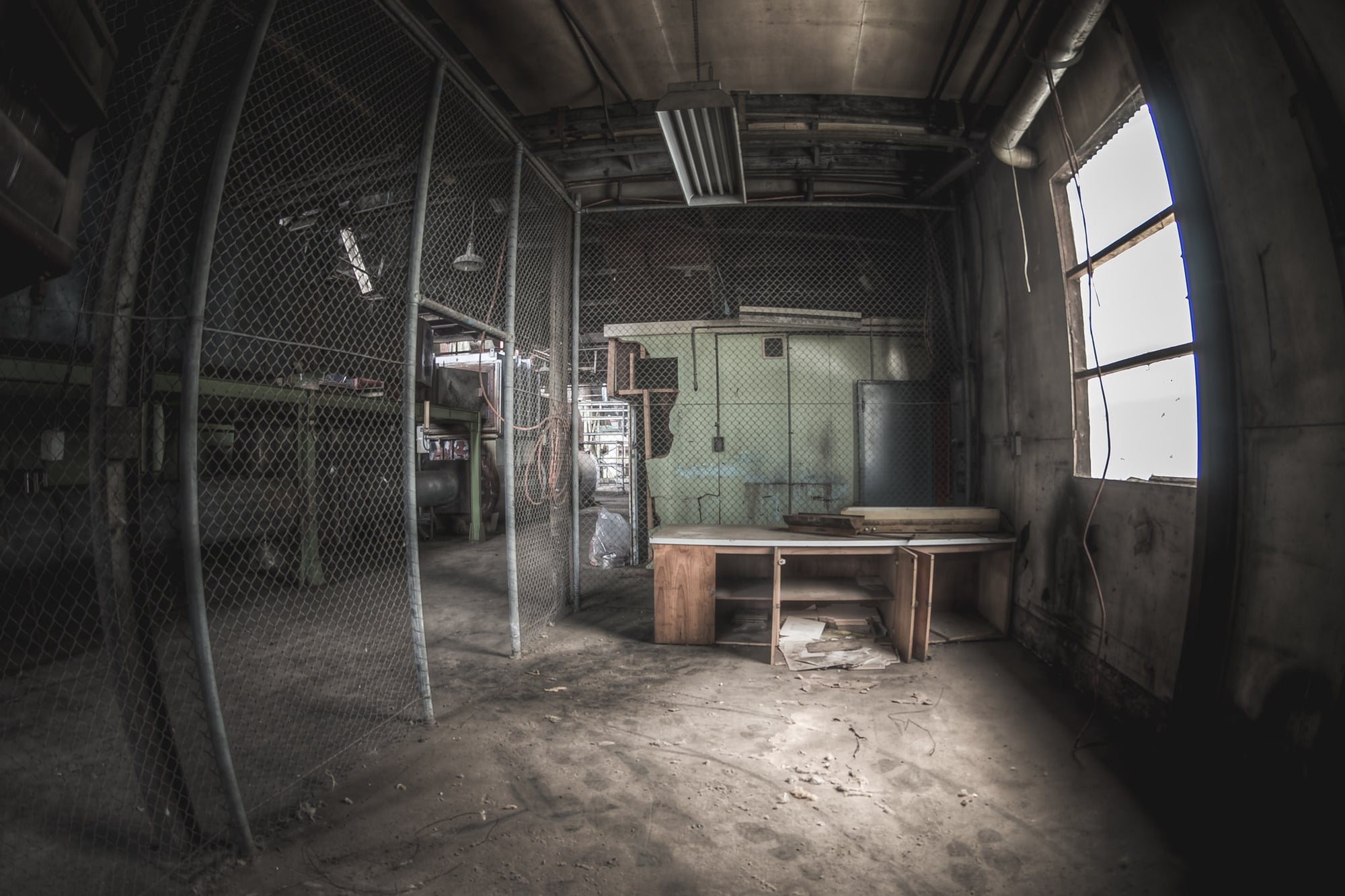 Caged Area at O-I Glass, a wooden desk sits near a large arched window, grey light falling across its surface.