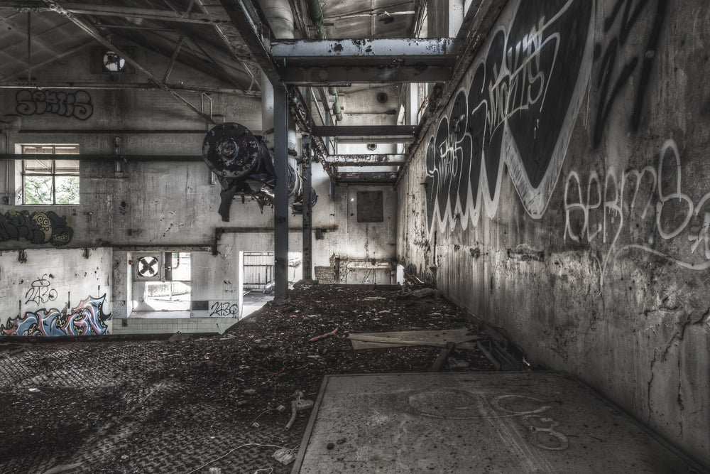 Concentrate Room Mezzanine at Peters Ice Cream Factory, a heavy motor assembly hangs from a steel I-beam, suspended above a floor thick with compacted debris and dirt.