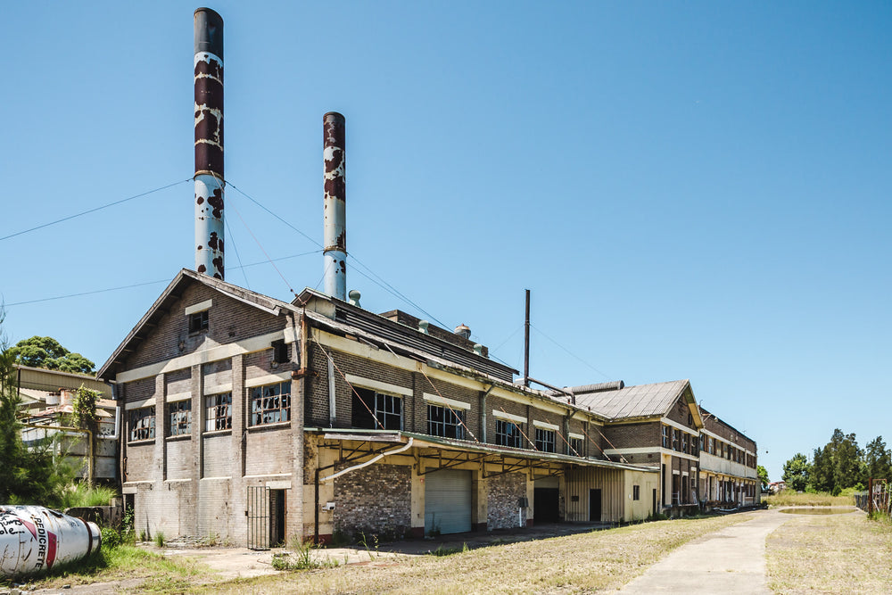 Engine Room Facade at Peters Ice Cream Factory, two steel smokestacks rise above the engine room block, their pale blue paint peeling away in large patches to expose dark rust beneath.
