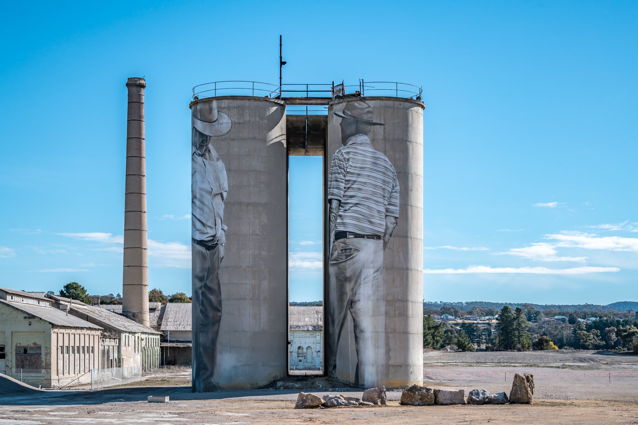 Between Silos at Portland Cement Works, two concrete silos stand side by side on bare ground, a narrow vertical gap cut.