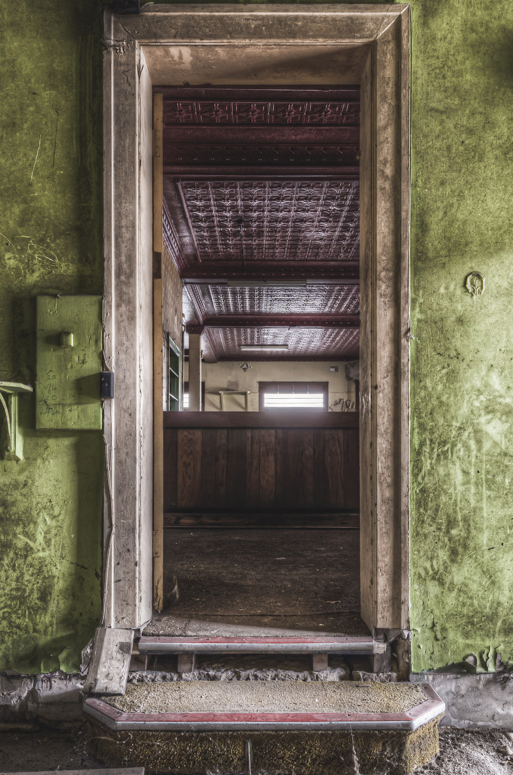 Bar Entrance at Terminus Hotel, a worn step rises to meet the barroom threshold, framed by peeling green paint and chipped.