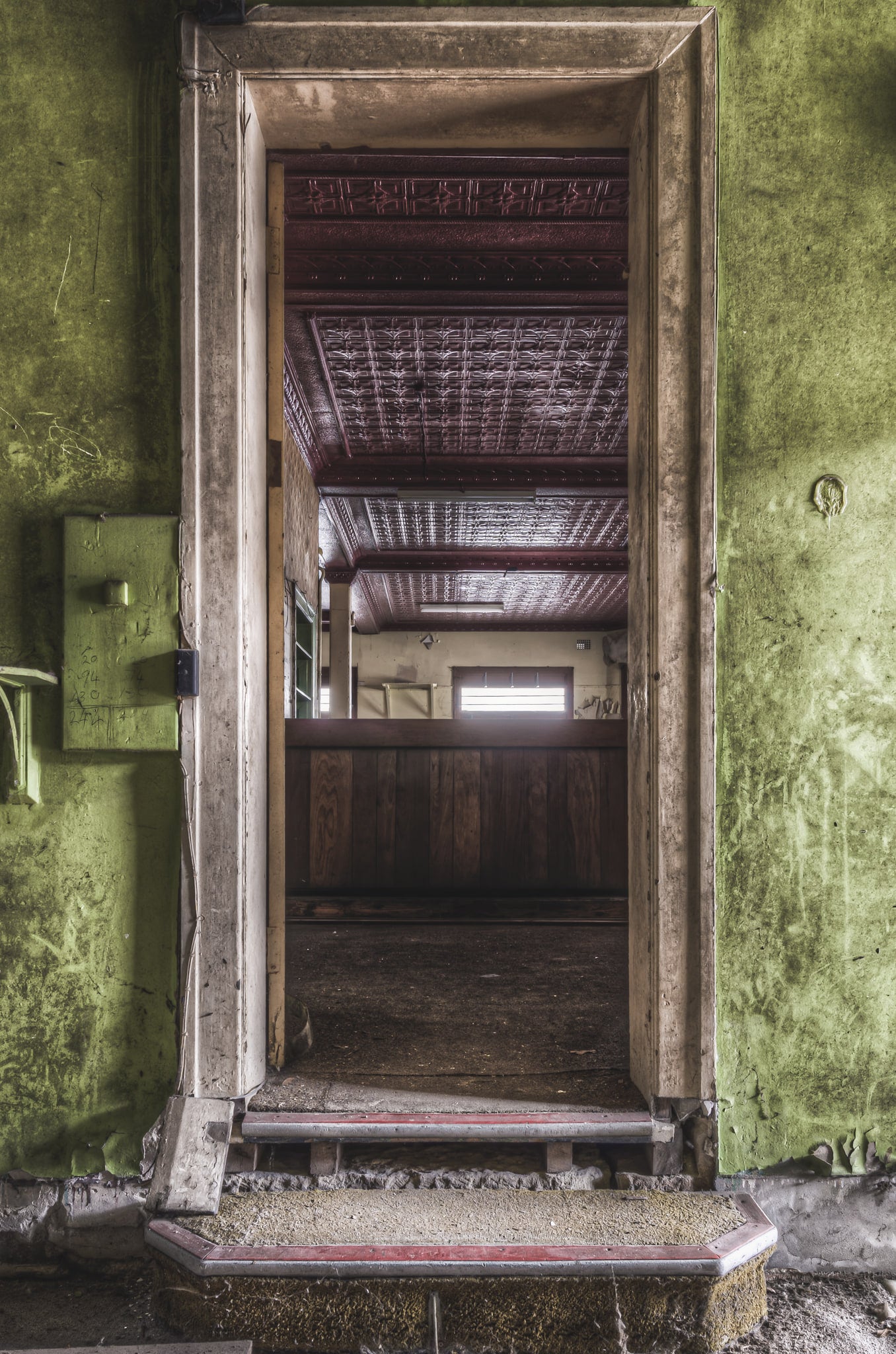 Bar Entrance at Terminus Hotel, a worn step rises to meet the barroom threshold, framed by peeling green paint and chipped.